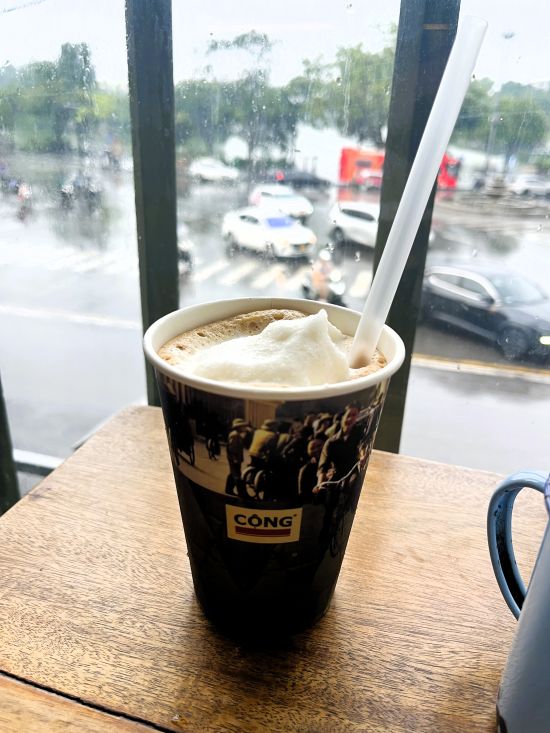Coconut coffee beside an upstairs window overlooking a rainy Hanoi street