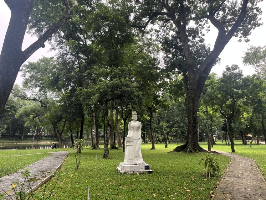 Shaded path and sculpture beneath large trees in Hanoi Botanical Gardens