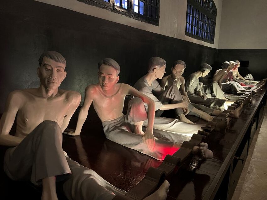 Exhibit showing prisoner figures with ankles secured in stocks at Hoa Lo Prison in Hanoi