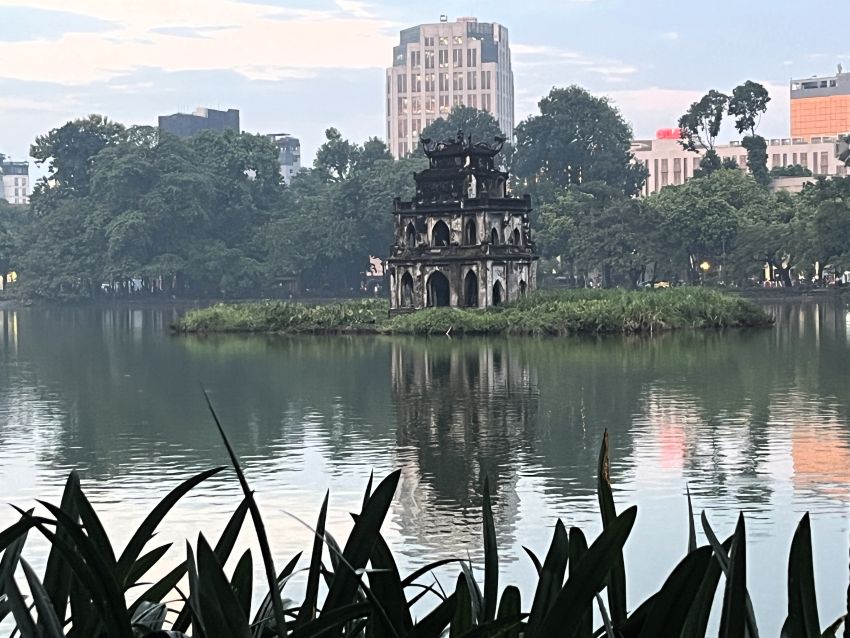 Turtle Tower reflected in Hoan Kiem Lake, with plants along the shore